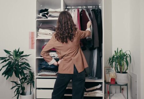 Frau steht vor Kleiderschrank und sortiert Kleidung aus. © Tchibo I Christopher Blank