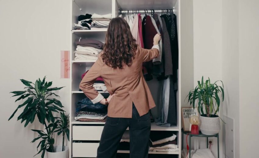 Frau steht vor Kleiderschrank und sortiert Kleidung aus. © Tchibo I Christopher Blank