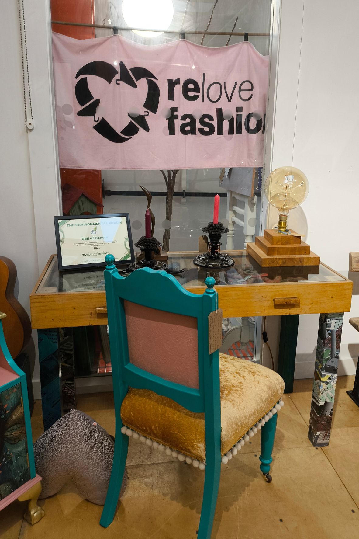 Bild zeigt einen alten Stuhl und Schreibtisch. Darüber ein Plakat mit der Aufschrift "relove fashion".