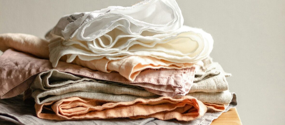 Bild zeigt mehrere Textilien unordentlich übereinander gestapelt auf einem Holztisch. (c) Svitlana on Unsplash