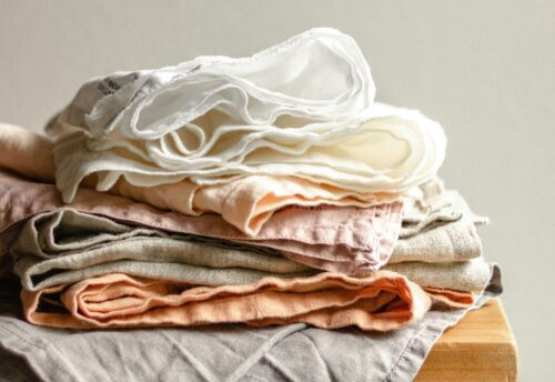 Bild zeigt mehrere Textilien unordentlich übereinander gestapelt auf einem Holztisch. (c) Svitlana on Unsplash