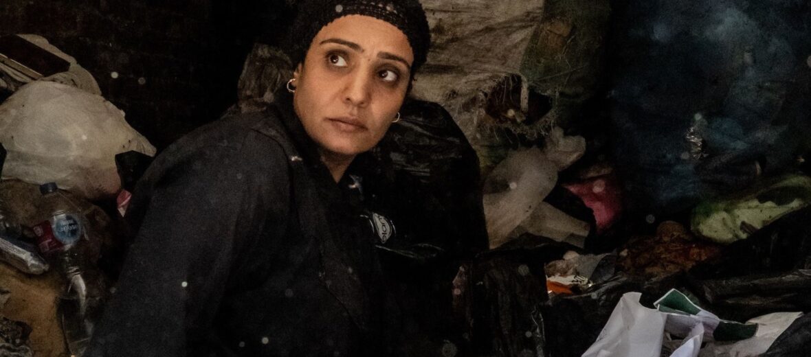 Bild zeigt eine Frau in schwarzer Kleidung vor einem Berg aus alter Textilien. (c) Ingmar Ostermaier)