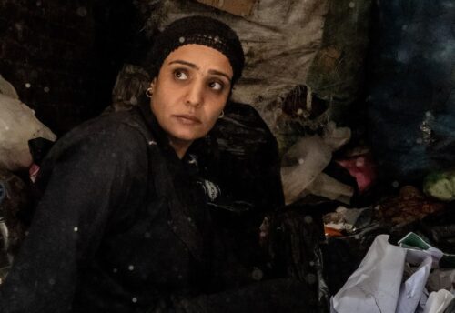 Bild zeigt eine Frau in schwarzer Kleidung vor einem Berg aus alter Textilien. (c) Ingmar Ostermaier)